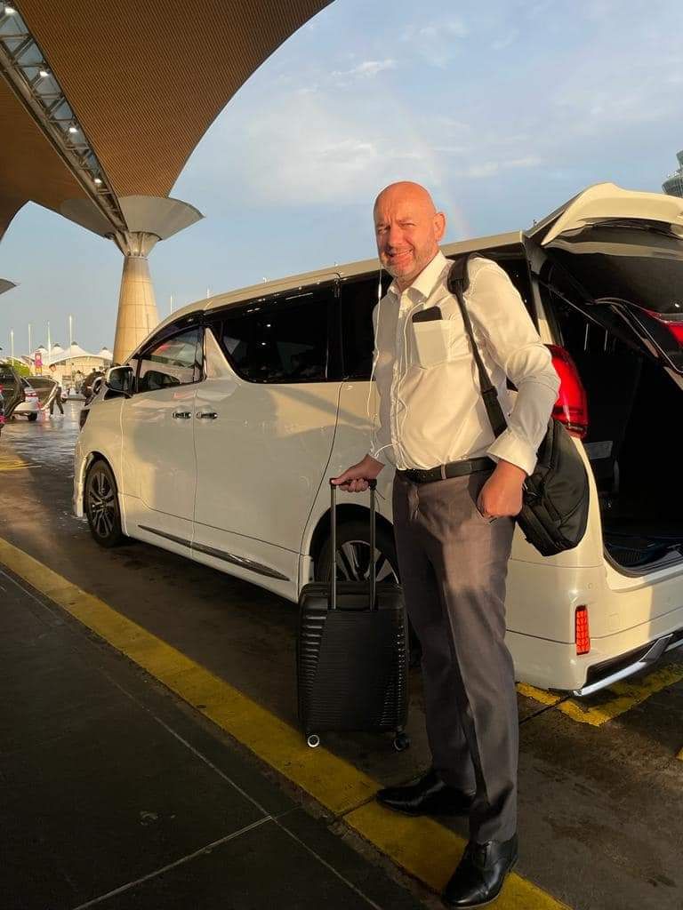 A traveller with a suitcase beside a white MPV